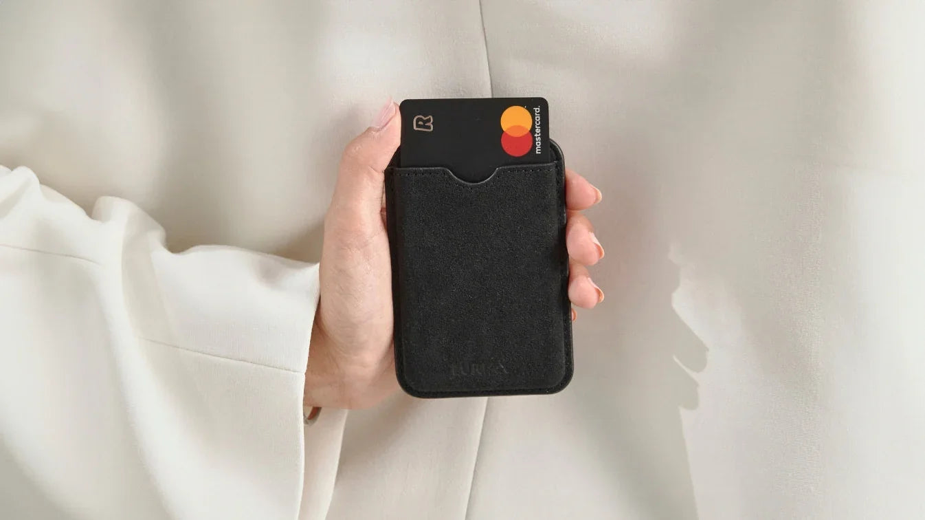 Luriax Pure Black Alcantara cardholder with suede-like texture, holding Mastercard, held in hand against white fabric.